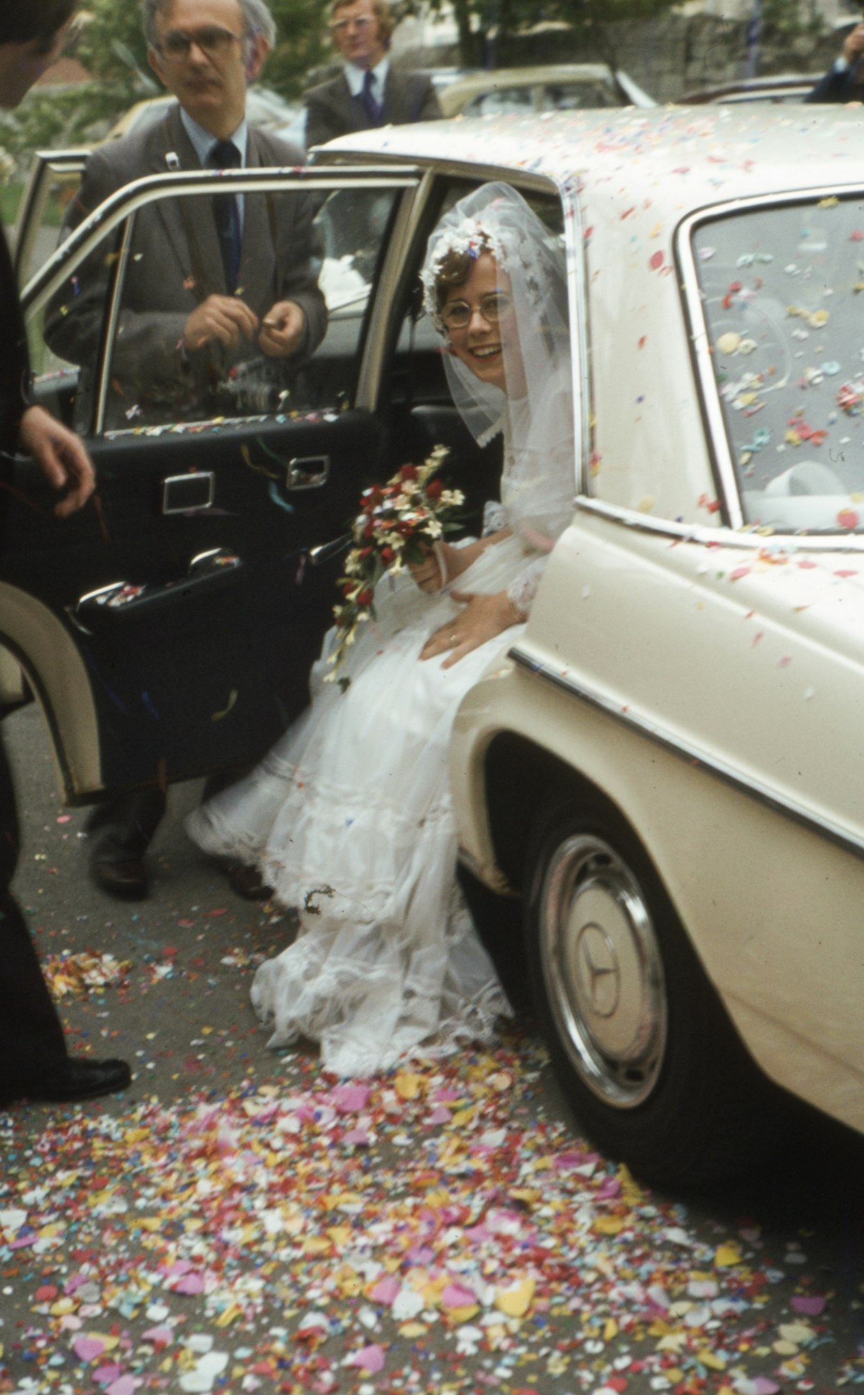 A bride stepping out of a vintage car into confetti